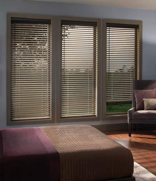 A bedroom with an armchair, long windows with metal window blinds and a custom bed.