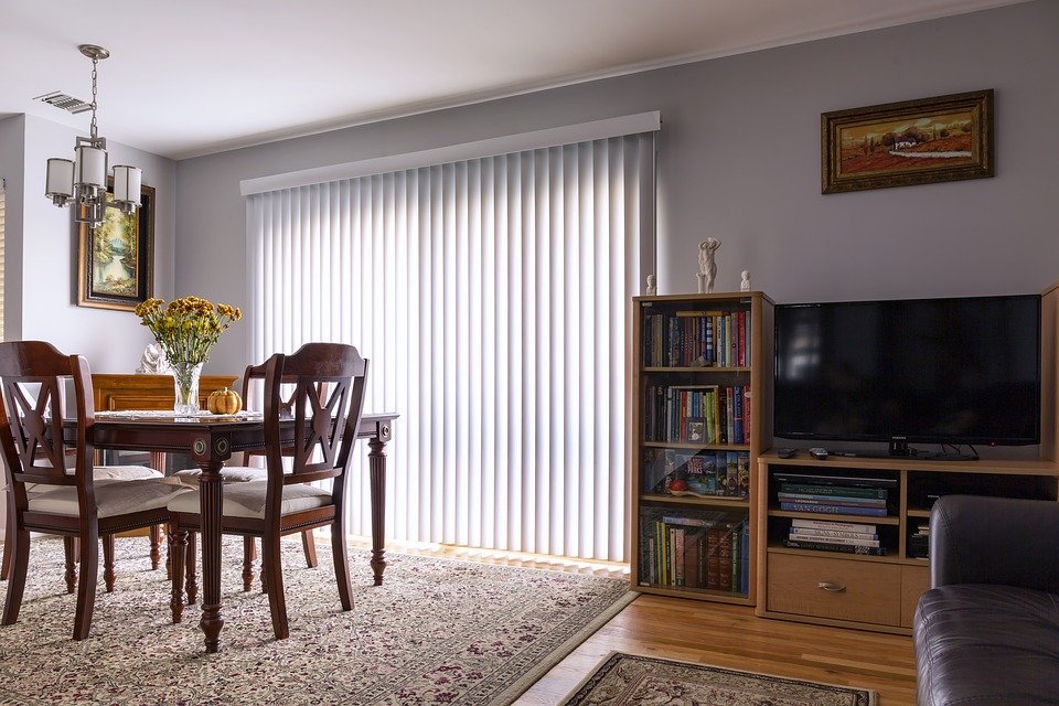 A living room with blinds, dining table, and a TV console